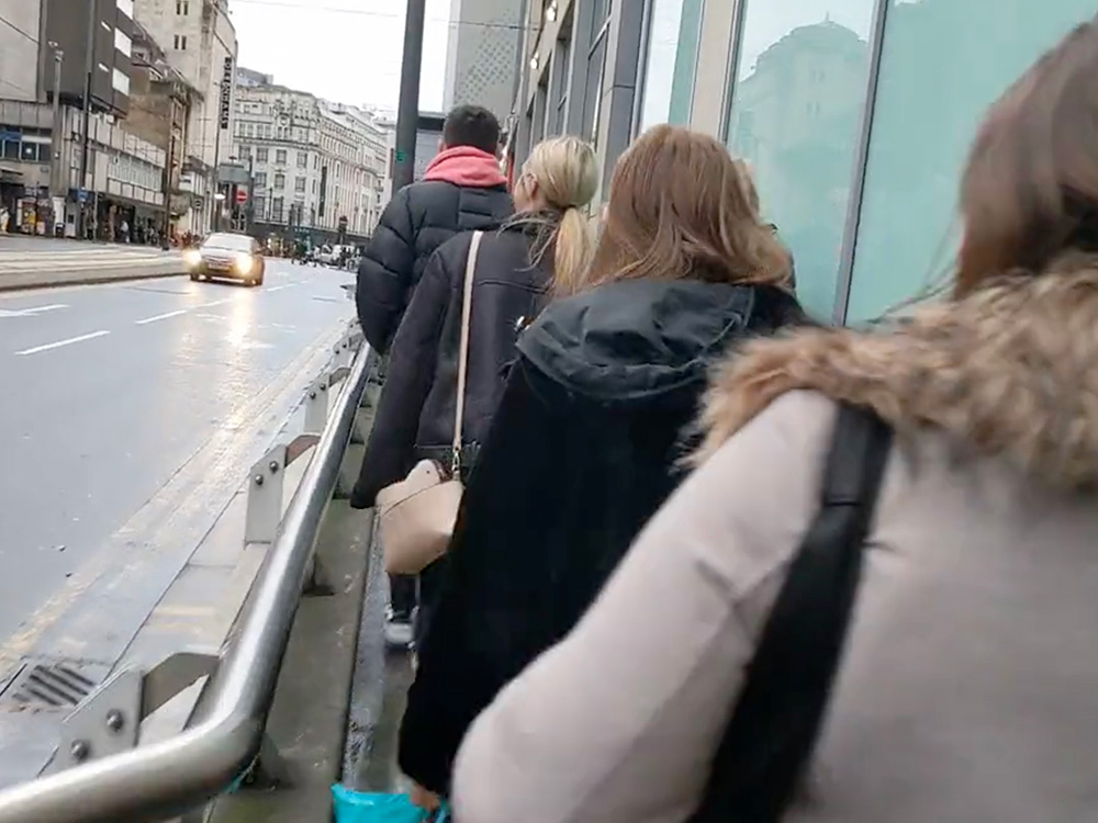 The left of the image shows High Street in central Manchester with one car driving down it. The right of the image shows a crowd of people walking in single file along a very narrow pavement.