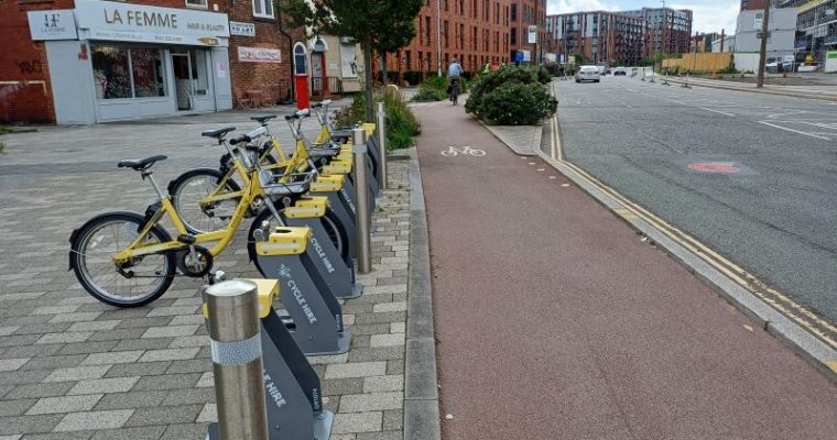 Oldfield Road cycleway in Salford featuring cycle hire docks and planting