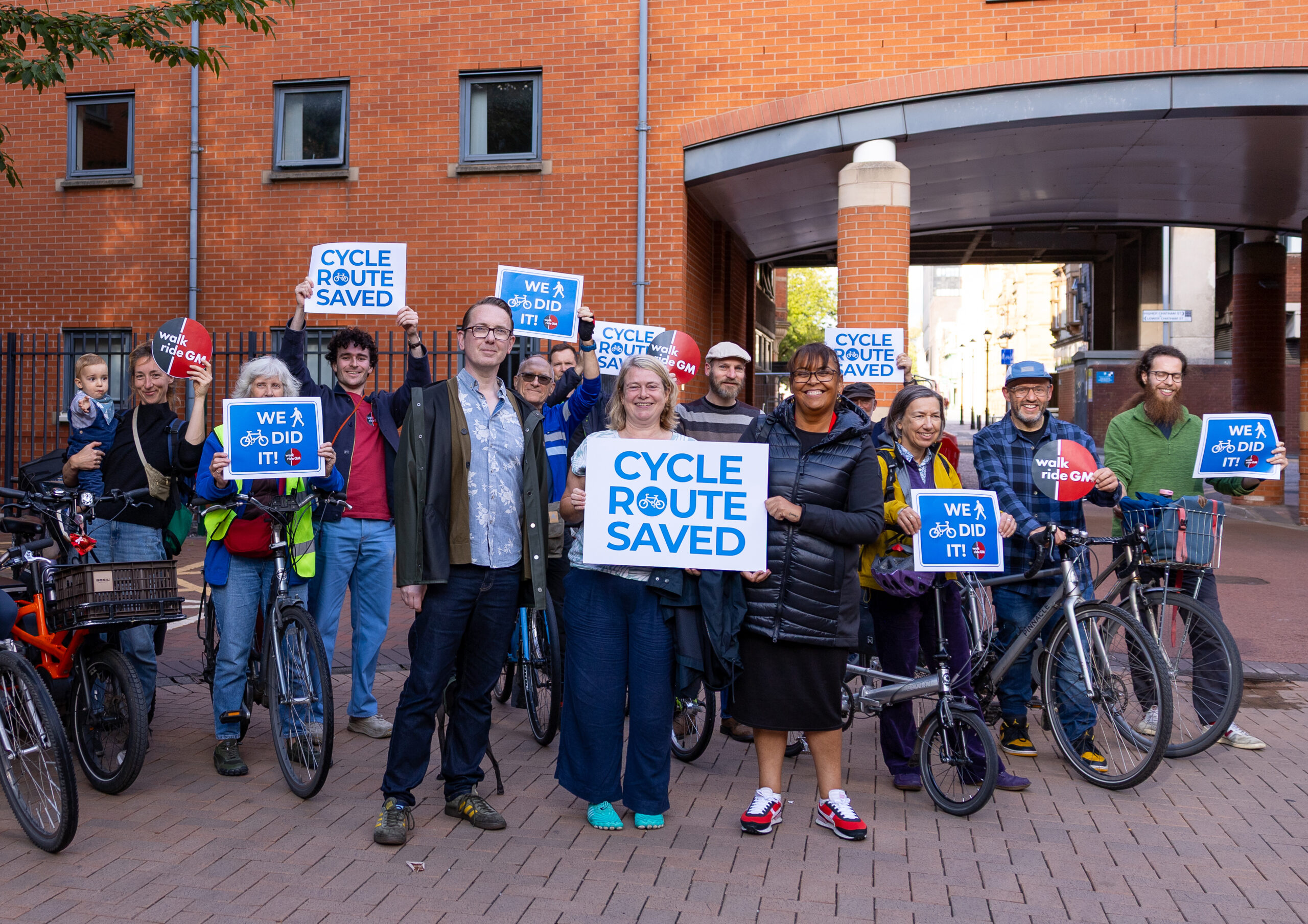 Members of Walk Ride GM and Hulme Councillors stood on Cavendish Street celebrating our campaign win to save the cycle route on MMU campus.