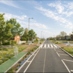 A CGI showing an impression of the proposals for a road. There are silhouettes of people walking, wheeling, sitting and cycling around. The road has trees, wildflower strips, houses, and cycle lanes running alongside, and a zebra crossing across the road in the near distance. There is a summery sky above.